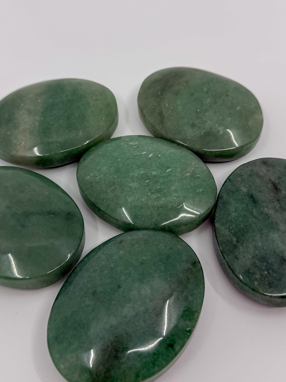 Five polished green aventurine oval palm stones arranged on a plain white background.